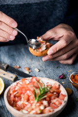 man topping a vegan appetizer with tomato salad