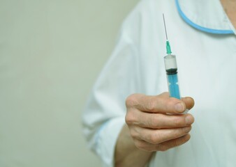 The hand of an elderly woman doctor holding a syringe on a white background, close-up.