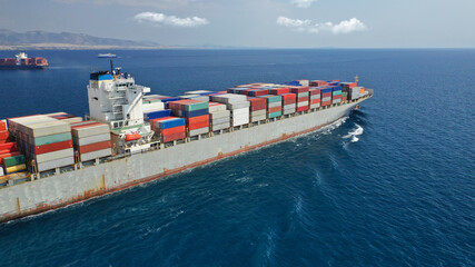 Aerial drone photo of huge container tanker ship carrying truck size colourful containers in deep blue open ocean sea