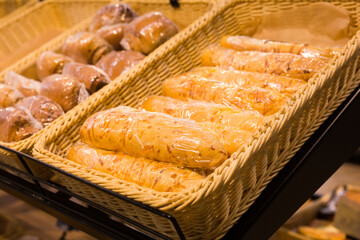 fresh golden breads with melted cheese wrapped in plastic wrap in wicker basket in bread department of supermarket