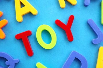 The word Toy is laid out in colored plastic letters of the English alphabet on a blue background.