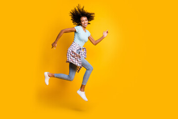 Fototapeta na wymiar Photo of sweet charming dark skin curly woman dressed blue t-shirt jumping running fast isolated yellow color background