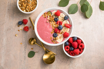 Summer acai smoothie bowls with raspberries, banana, blueberries, and granola on gray concrete background. Breakfast bowl with fruit and cereal, close-up, top view, space for text