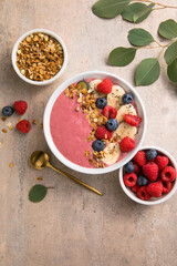 Summer acai smoothie bowls with raspberries, banana, blueberries, and granola on gray concrete background. Breakfast bowl with fruit and cereal, close-up, top view, space for text