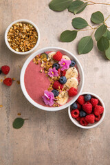 Summer acai smoothie bowls with raspberries, banana, blueberries, and granola on gray concrete background. Breakfast bowl with fruit and cereal, close-up, top view, space for text