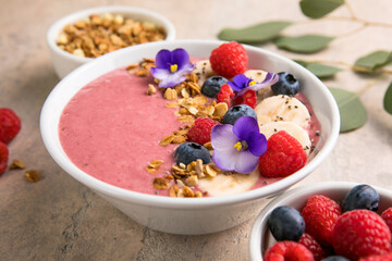 Summer acai smoothie bowls with raspberries, banana, blueberries, and granola on gray concrete background. Breakfast bowl with fruit and cereal, close-up, top view, space for text
