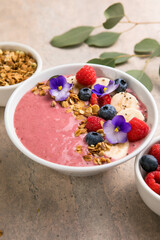 Summer acai smoothie bowls with raspberries, banana, blueberries, and granola on gray concrete background. Breakfast bowl with fruit and cereal, close-up, top view, space for text