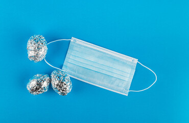 Medical protective mask and Eggs in aluminum foil on blue background.