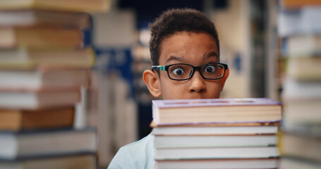 Close up of african kid feeling shocked looking at large stack of book on table