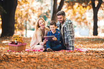 Happy family having picnic in park, using digital tablet.