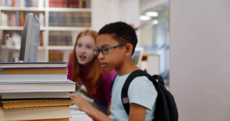 Diverse kids searching for book in e-catalog on computer in library