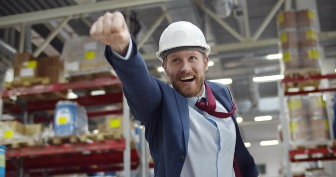 Portrait of superhero businessman in hardhat and formal suit in warehouse