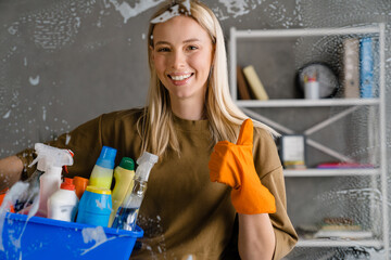 Blonde woman maid holding basket full of cleaning products