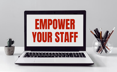 Laptop with EMPOWER YOUR STAFF text on modern office background.