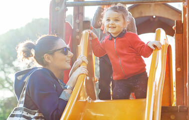 Aunt and nephew play on the slide at the park.