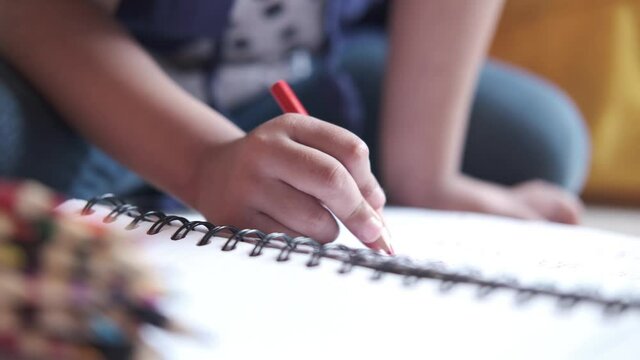 Close up of a child hand drawing with colored pencil on a page.