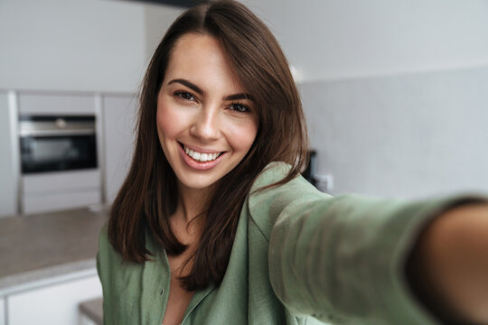 Young happy woman smiling while taking selfie photo at home kitchen