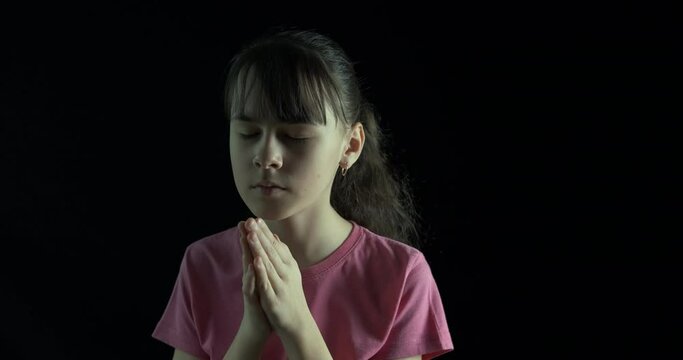 The child is praying. Teenage girl praying on a black background.