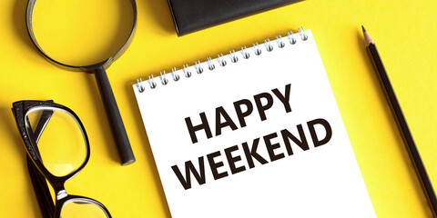 Notepad with the text happy weekend on a yellow background with glasses, a magnifying glass and a pencil