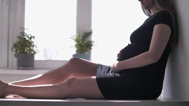 Pregnant Woman Sitting in Black Dress Against the Window