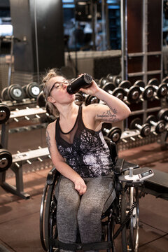Woman on wheelchair drinking water in gym