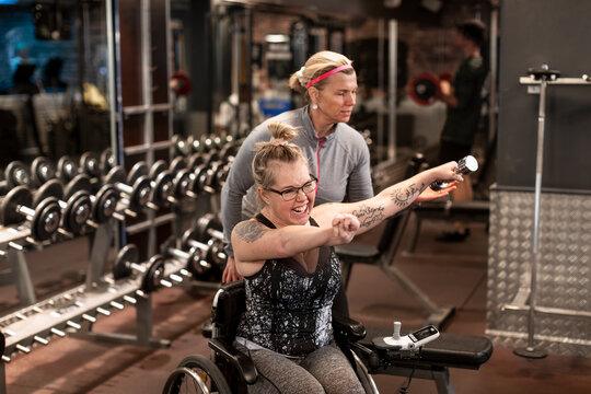 Happy woman on wheelchair training in gym with personal trainer