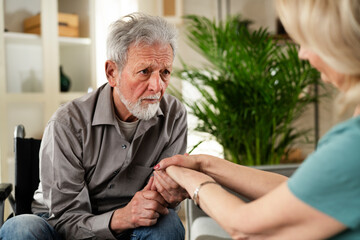 Senior man in wheelchair. Wife comforting her sad husband.