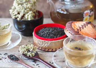 Composition of Asian medicinal herbal tea. A box with natural leaves of a tea plant, a medicinal herb and a teapot with a tea cup of brewed drink.