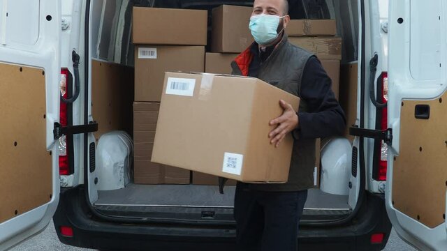 Young man shipper with his van during the delivery round in the global pandemic from Covid-19 Coronavirus wearing face mask while checking address with smartphone
