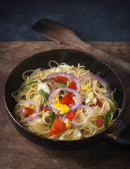 cooked spaghetti dish with egg, tomatoes, onions and green chilies on a pan, spaghetti pasta dish
on a dark background