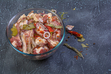 Pork ribs, sliced and marinated with onions. Shish Kebab meat in a glass bowl and spices on a textured background.Selective focus, close-up, top view.Homemade food.