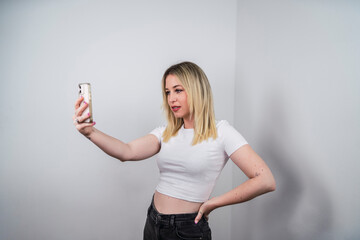 Chica rubia risueña usando smartphone y sonriendo sobre fondo blanco