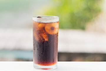 Full glass of Coca-Cola water with ice with water droplets around the glass, refreshing chilled drink, green natural backdrop.