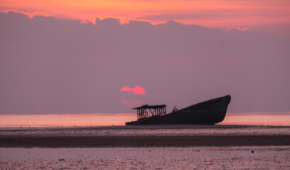 A silhouette shipwreck on the beach and sunrise in the morning