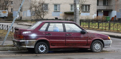 Old red abandoned passenger car with flat wheels in the courtyard of a residential building, Iskrovsky Prospekt, Saint Petersburg, Russia, March 2021