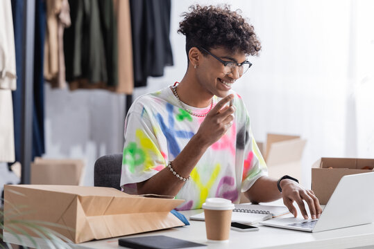 Smiling African American Small Business Owner Using Laptop Near Takeaway Drink And Packages