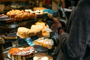 Confectionery customer, client in sweet-shop, pastry-shop. Back view of young woman choosing cake desserts from display in confectionery, shop, cafe.