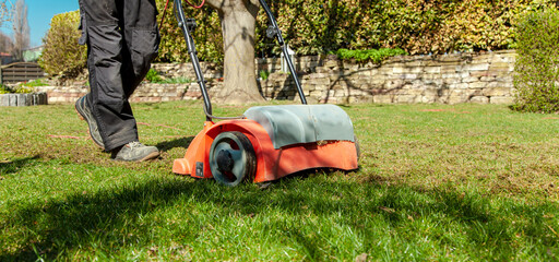 Using a scarifier in the garden to improving quality of the lawn in spring. male worker man,...