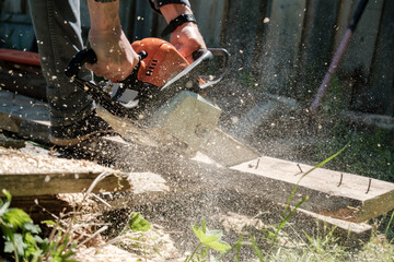 Male hands sawing old boards for firewood with a professional chainsaw, in a village yard. Winter preparation concept. Lifestyle.