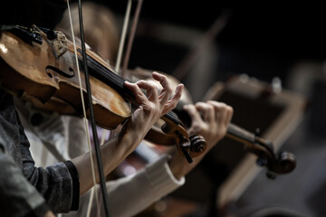 Violinists' hands in a symphony orchestra in dark colors