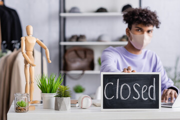 Chalkboard with closed lettering near african american businessman in protective mask in showroom...