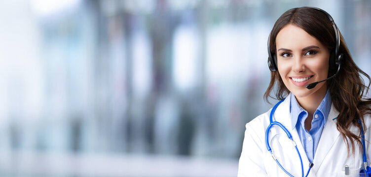 Portrait of happy smiling female doctor in headset, over blurred modern office background, copy space area for slogan or text. Medical call center concept picture.