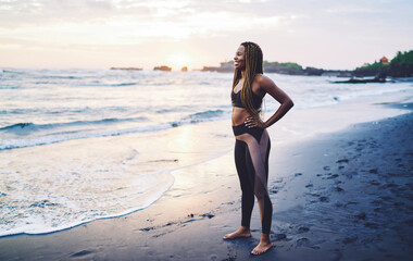 Cheerful African American woman feeling happiness during morning training at coastline looking away and smiling, funny dark skinned jogger dressed in sportive clothes clothes laughing at seashore