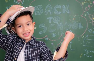Asian little boy wear white engineer hat on blackboard.