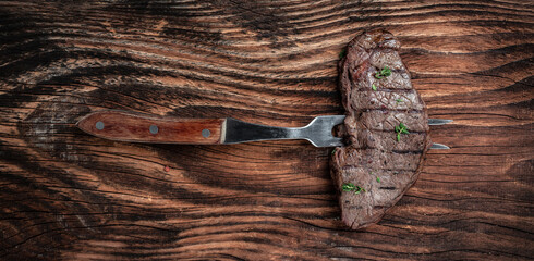 Rump Steak on fork on dark wooden background. banner, menu recipe place for text, top view