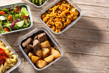 Take away healthy food in foil boxes on wooden table. Copy space