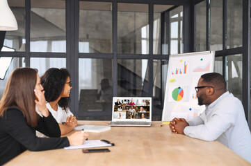 Multiracial work team using app on the laptop for connect with colleagues on the distance, a group of employee sits at modern coworking involved in video meeting, video conference, brainstorming