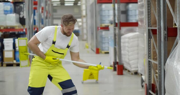Funny male janitor dancing with mop in warehouse