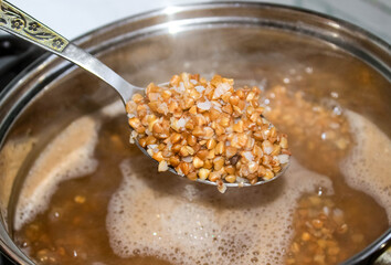 Buckwheat in a spoon on the background of a pan with buckwheat groats.