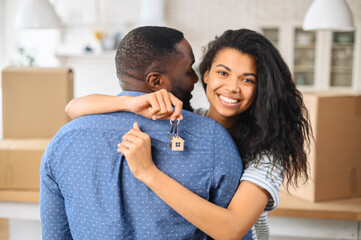 Hilarious biracial woman embraces black man and holds keys with trinket in form of cute wooden...